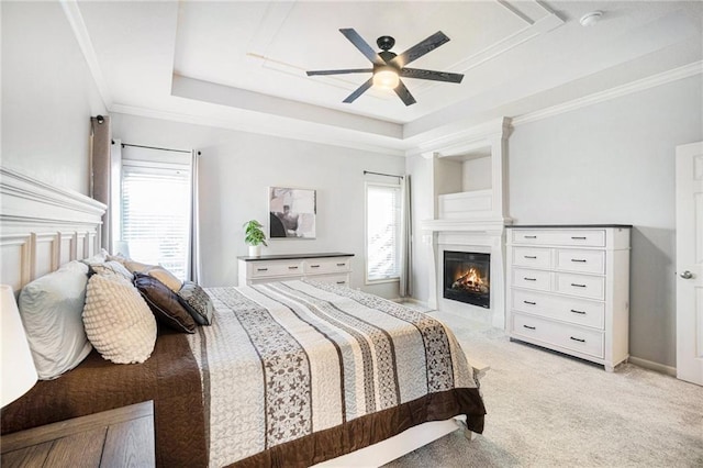 bedroom with a tray ceiling, multiple windows, light carpet, and a glass covered fireplace