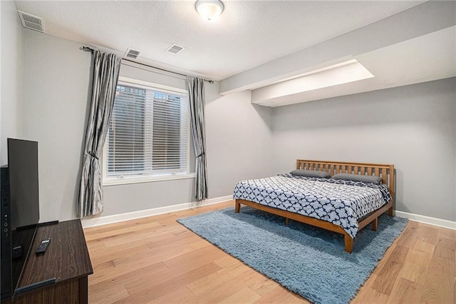 bedroom with wood finished floors, visible vents, and baseboards