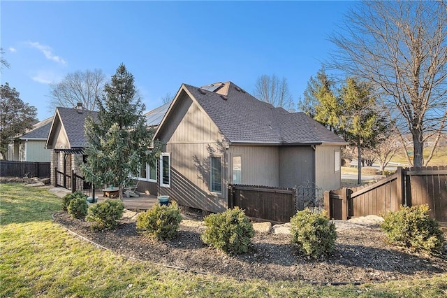 back of property with a lawn, a shingled roof, and fence