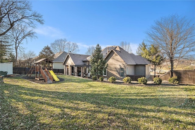 back of property with a playground, a yard, and fence