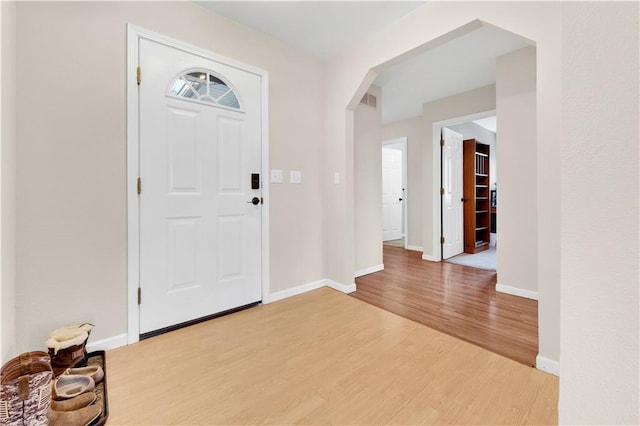 entryway with light wood-style floors, arched walkways, and baseboards