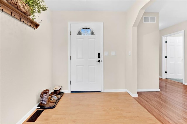 entryway with arched walkways, light wood-type flooring, visible vents, and baseboards