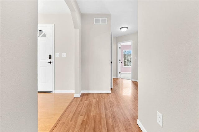 hallway with baseboards, visible vents, and light wood finished floors