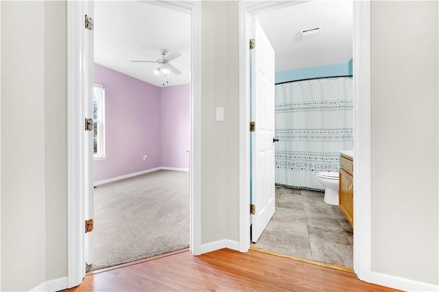 corridor featuring baseboards, light carpet, and light wood finished floors