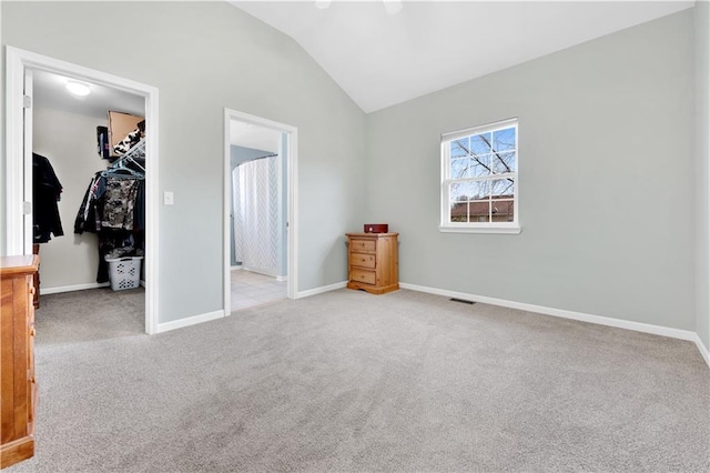 unfurnished bedroom featuring baseboards, light colored carpet, vaulted ceiling, a walk in closet, and a closet