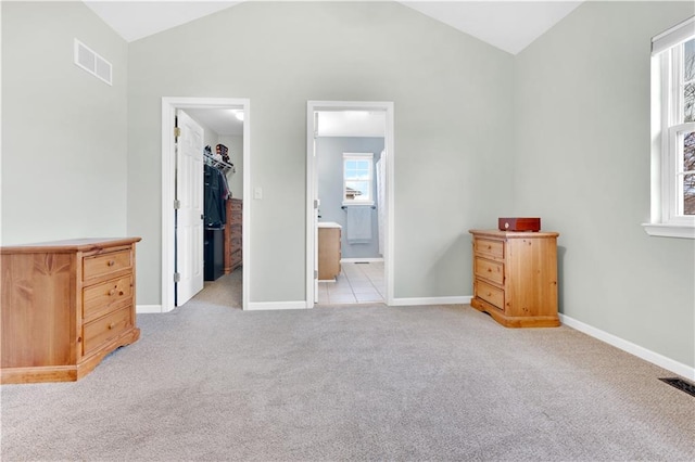 unfurnished bedroom with a walk in closet, visible vents, light carpet, vaulted ceiling, and baseboards