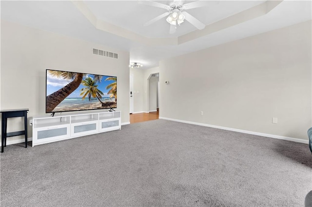 unfurnished living room featuring a tray ceiling, visible vents, carpet flooring, ceiling fan, and baseboards