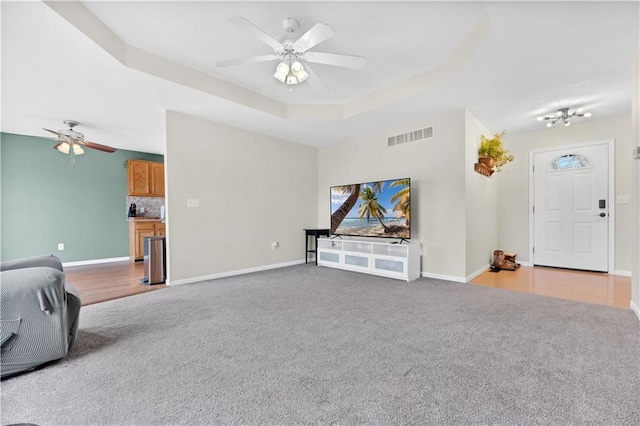 unfurnished living room with ceiling fan, carpet flooring, visible vents, baseboards, and a raised ceiling