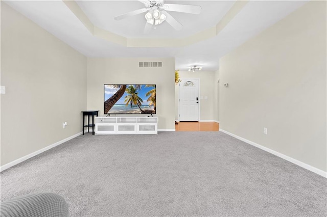 unfurnished living room featuring a ceiling fan, visible vents, baseboards, a tray ceiling, and carpet