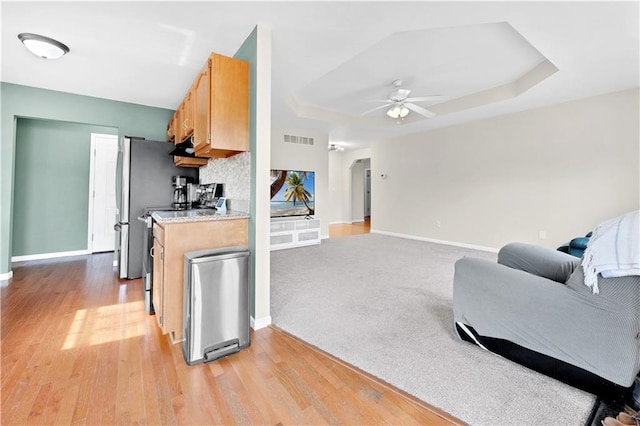 kitchen featuring a tray ceiling, light countertops, visible vents, light wood-style floors, and ceiling fan