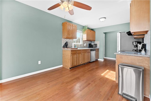 kitchen featuring light wood-style flooring, stainless steel appliances, a sink, light countertops, and decorative backsplash