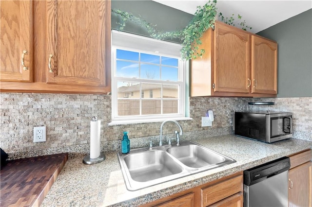 kitchen with appliances with stainless steel finishes, light countertops, a sink, and backsplash