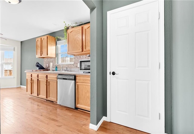 kitchen with light countertops, stainless steel dishwasher, light brown cabinetry, light wood-style floors, and backsplash