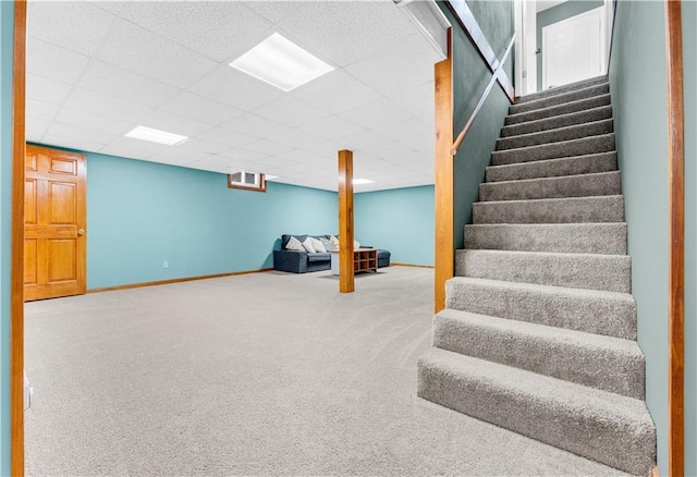 finished basement featuring a paneled ceiling, carpet, stairs, and baseboards