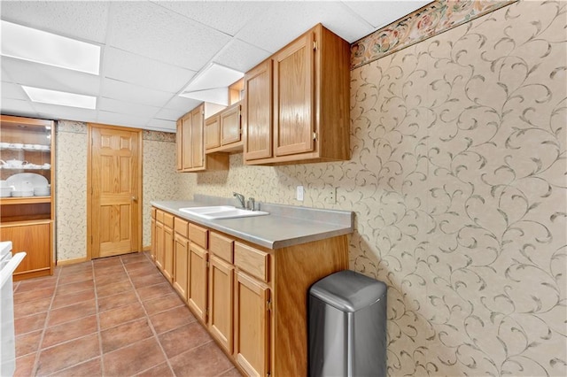 kitchen featuring light countertops, light tile patterned flooring, a sink, a drop ceiling, and wallpapered walls