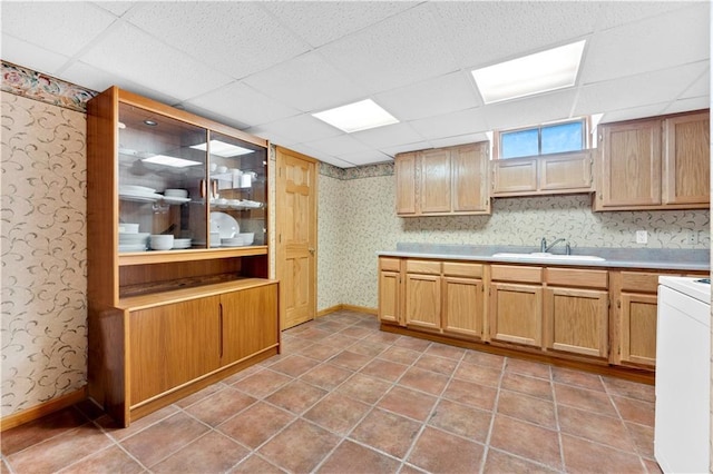 kitchen featuring light countertops, a drop ceiling, a sink, and wallpapered walls