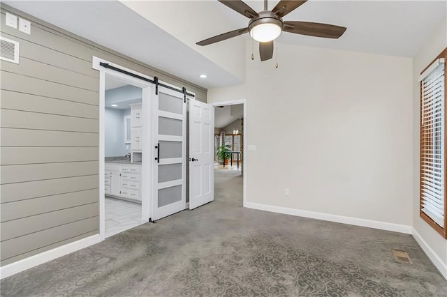 empty room featuring a barn door, baseboards, lofted ceiling, and ceiling fan