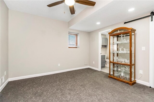 carpeted empty room featuring a barn door, baseboards, a textured ceiling, and ceiling fan