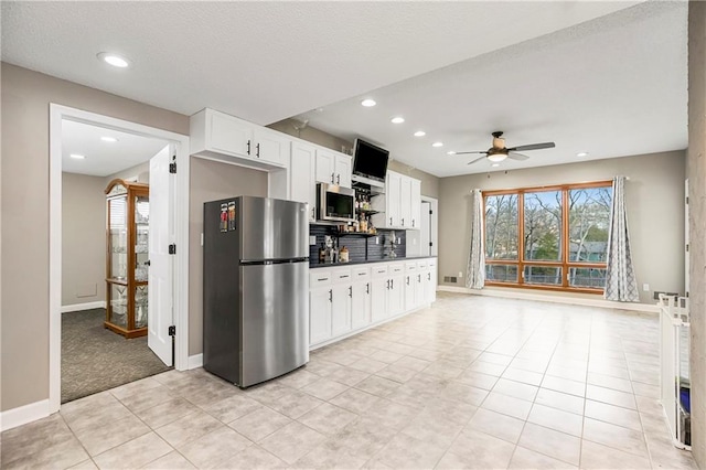 kitchen with a ceiling fan, baseboards, stainless steel appliances, white cabinetry, and dark countertops