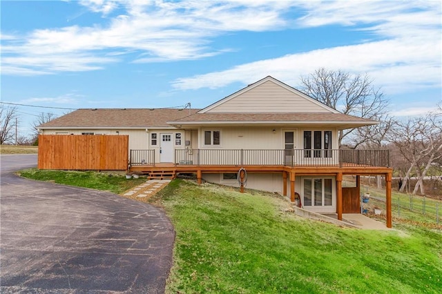 back of property featuring a lawn, a shingled roof, a deck, and fence