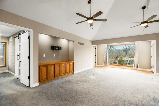 unfurnished living room with a barn door, carpet flooring, visible vents, and plenty of natural light