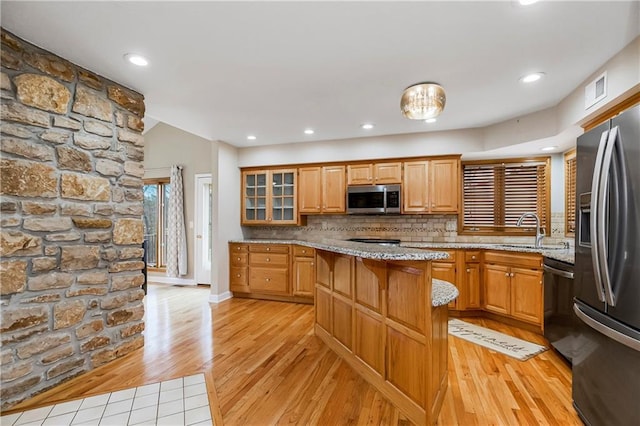 kitchen with light wood finished floors, stainless steel appliances, light stone counters, and a sink