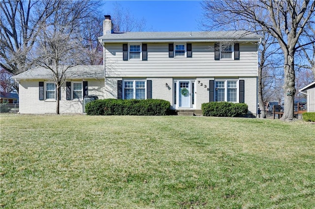 colonial inspired home with brick siding, a chimney, a front lawn, and fence