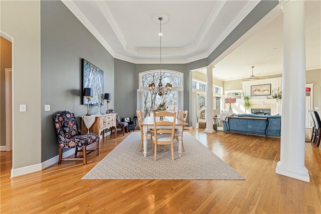 dining room with a tray ceiling, light wood-style floors, crown molding, and ornate columns