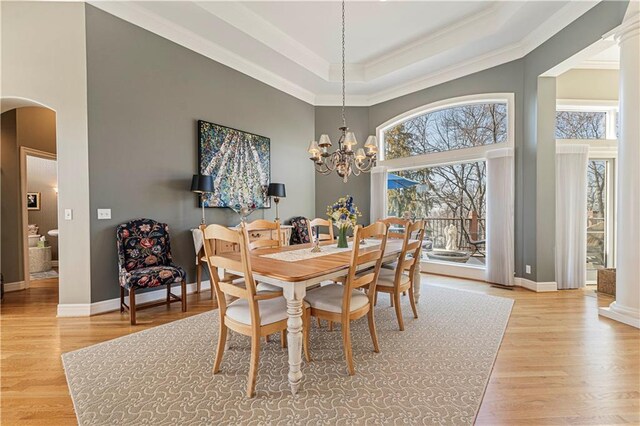 dining space featuring arched walkways, light wood finished floors, a raised ceiling, and baseboards