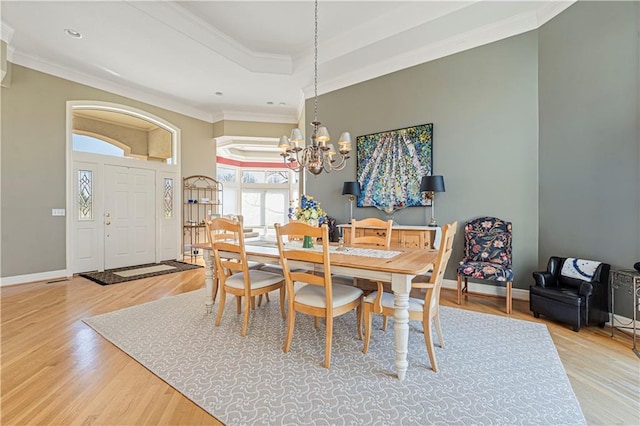 dining room featuring light wood-style floors, a raised ceiling, crown molding, and an inviting chandelier