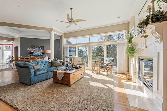 living room with light wood finished floors, ceiling fan with notable chandelier, crown molding, and decorative columns