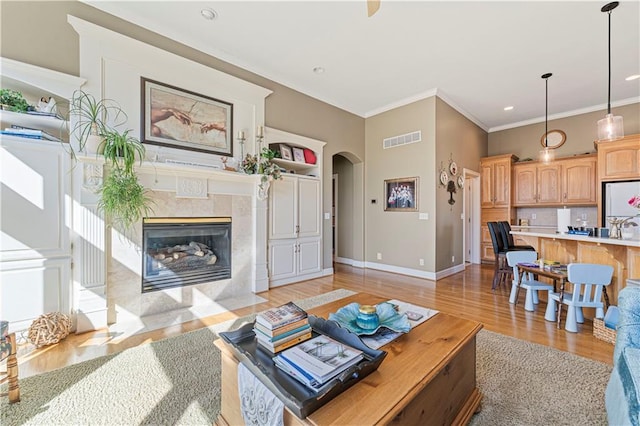living area featuring light wood finished floors, visible vents, crown molding, baseboards, and arched walkways