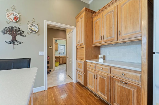kitchen featuring backsplash, baseboards, light countertops, light wood-style floors, and a sink
