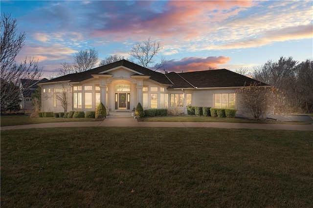 ranch-style home with curved driveway, a front lawn, and stucco siding