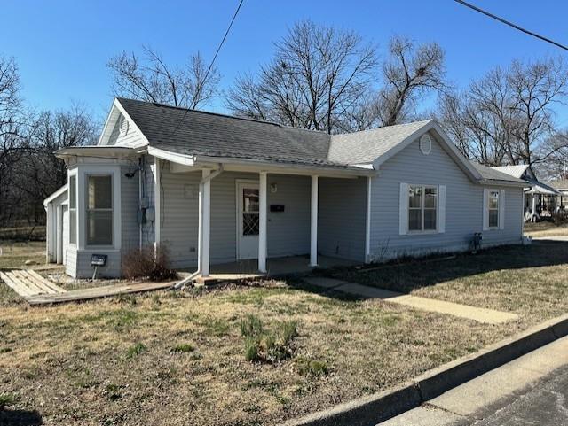 view of front of home with covered porch, a front lawn, and roof with shingles