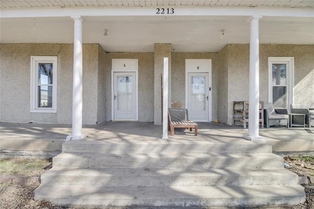 view of exterior entry with a porch and stucco siding