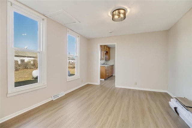 spare room with light wood-style floors, baseboards, visible vents, and attic access