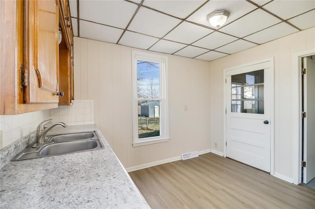 kitchen with a sink, visible vents, light wood-style floors, light countertops, and backsplash