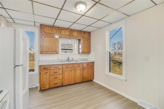 kitchen with brown cabinetry, freestanding refrigerator, light countertops, and a sink