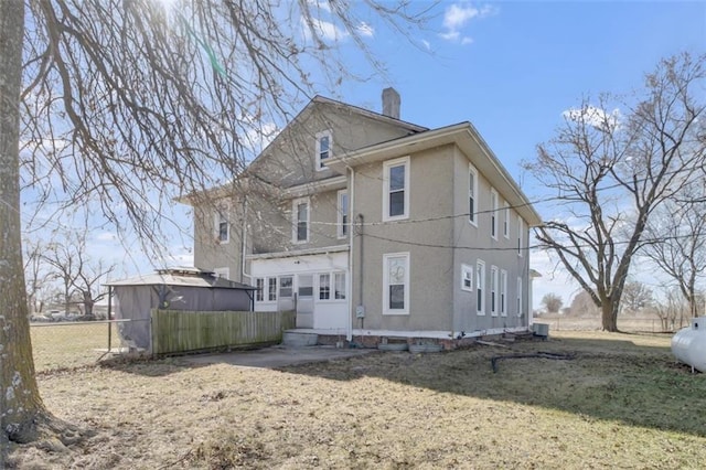 back of house with a chimney, fence, and stucco siding