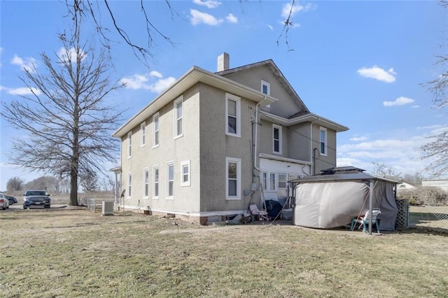 back of property with central AC, a yard, a chimney, and stucco siding