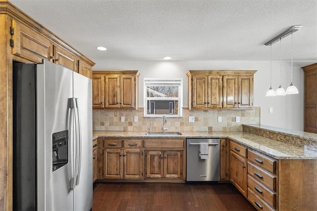 kitchen featuring a peninsula, a sink, appliances with stainless steel finishes, brown cabinetry, and decorative light fixtures