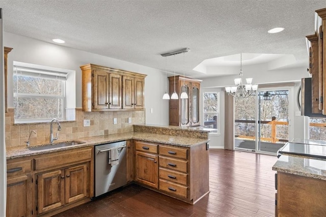 kitchen featuring pendant lighting, a raised ceiling, a sink, dishwasher, and a peninsula