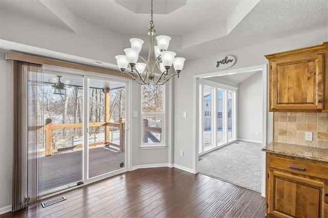 unfurnished dining area featuring a tray ceiling, dark wood finished floors, visible vents, and plenty of natural light