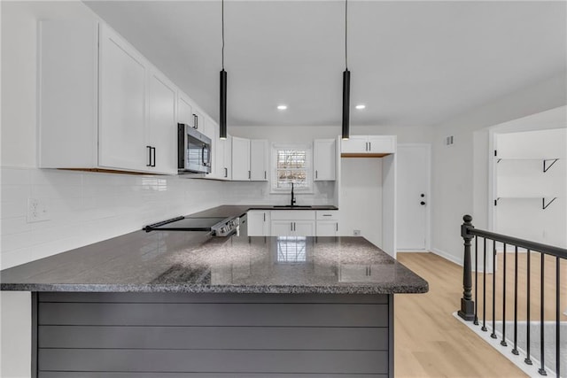 kitchen with white cabinetry, range, sink, and hanging light fixtures