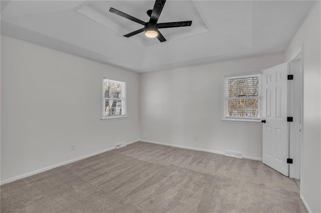 carpeted spare room featuring a healthy amount of sunlight, ceiling fan, and a tray ceiling