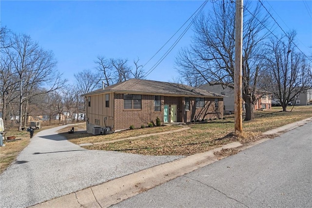 view of front of home with cooling unit, brick siding, board and batten siding, and driveway