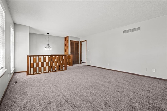 unfurnished room featuring visible vents, a textured ceiling, carpet, an inviting chandelier, and baseboards