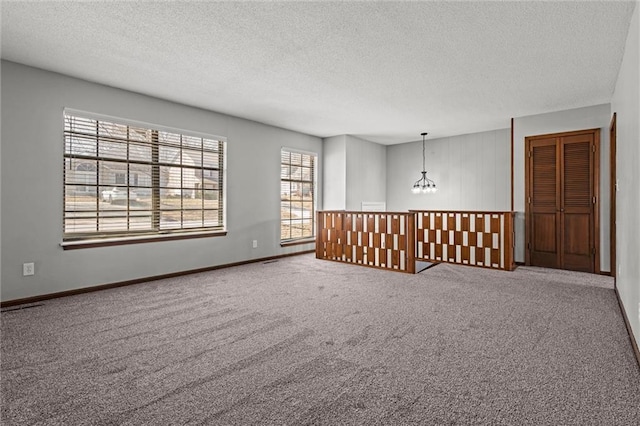 spare room featuring a notable chandelier, carpet flooring, a textured ceiling, and baseboards