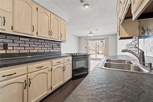 kitchen with dark countertops, light brown cabinetry, decorative backsplash, black range with gas cooktop, and a sink